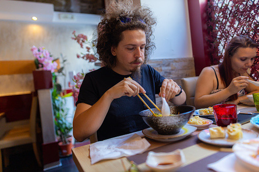 A shot of a Caucasian couple eating noodles and sushi at an Asian restaurant. Asian food concept.