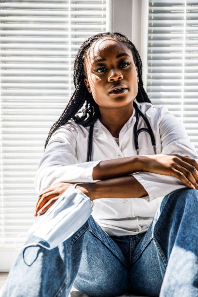 istock Overwhelmed female doctor sitting on the floor, looking away, pondering while taking a break from work 1455697833