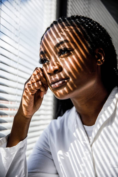 istock Female scientist standing by the window, blind shades playing on her face while she takes a break from work 1455697837
