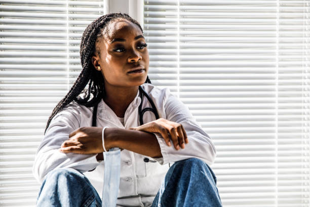 Overwhelmed female doctor sitting on the floor, looking away, pondering while taking a break from work
