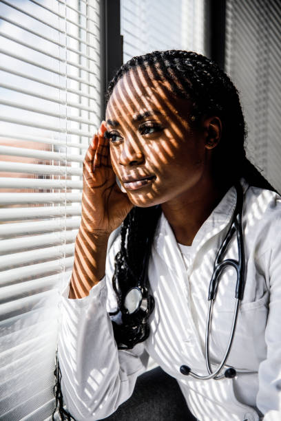 istock Female scientist standing by the window, blind shades playing on her face while she takes a break from work 1455697841