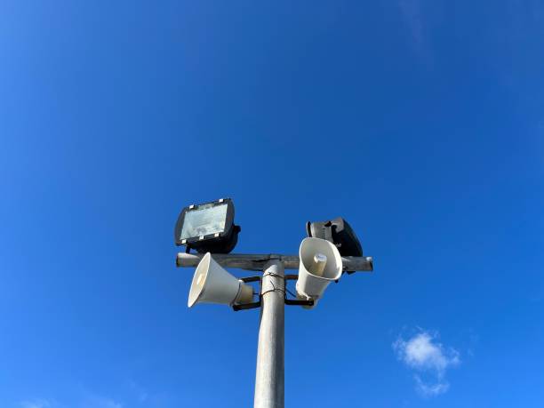 Speakers and lights suspended from a metal pole with blue sky