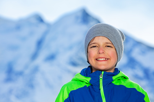 Close portrait of a smiling boy stand wearing wither coat and hat over mountain peaks