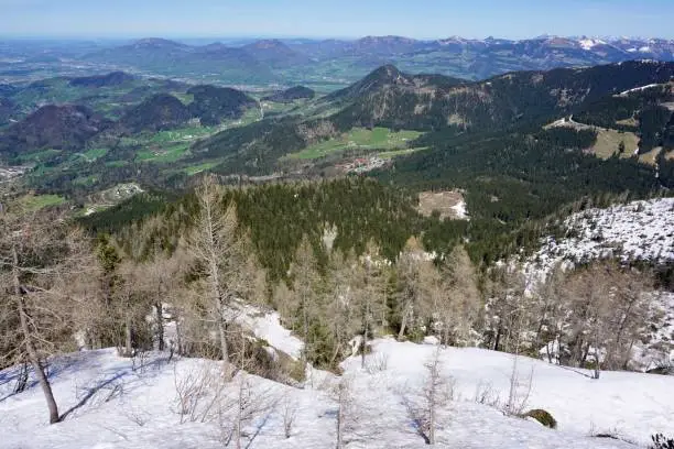 Top view of the Berchtesgaden valley. Panoramic view of the valley in Berchtesgaden from the Kehlstein height. View from the Bavarian Alps down to the green valley. Winter meets spring. Snow-capped peaks of mountains and greenery below.