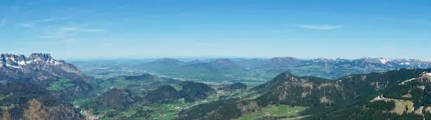Top view of the Berchtesgaden valley. Panoramic view of the valley in Berchtesgaden from the Kehlstein height. View from the Bavarian Alps down to the green valley. Winter meets spring. Snow-capped peaks of mountains and greenery below.