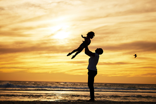 Sunset, silhouette and father with child at the beach with love and care on summer vacation. Playful, freedom and man playing with his kid in nature by ocean or sea on holiday, adventure or journey.