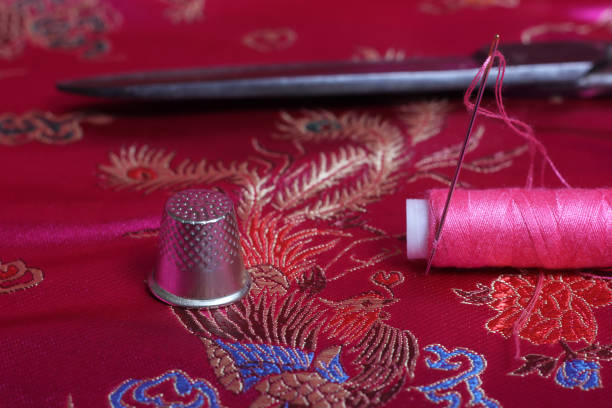 istock Spool of Pink Thread and Thimble on Vintage Pink Satin Fabric 1455704376
