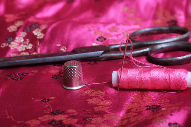 istock Spool of Pink Thread and Thimble on Vintage Pink Satin Fabric 1455704384
