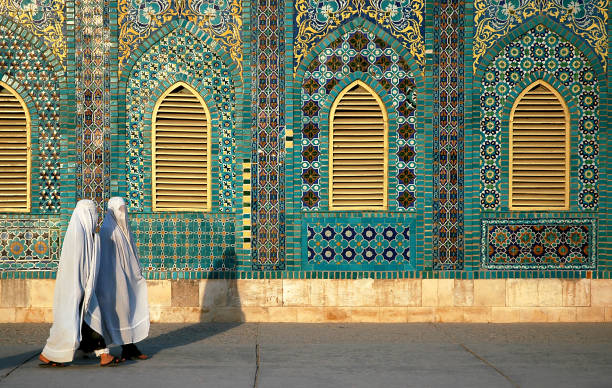 zwei frauen in weißen burkas (burkas) gehen an der blauen moschee in mazar-i-sharif, provinz balkh, afghanistan vorbei - mazar stock-fotos und bilder