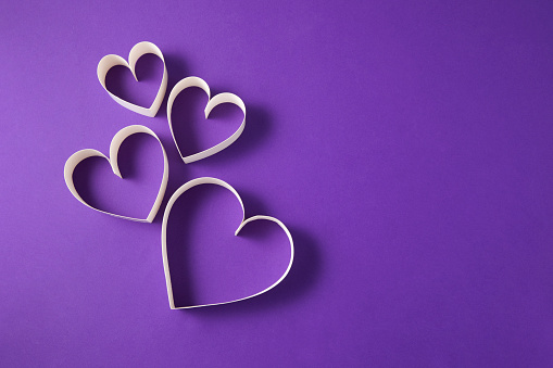 Heart shaped papers on purple background with copy space