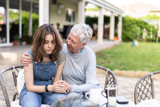 Grandsma's advice is the best A silvery haired grandmother is cuddling her sad granddaughter sitting outside in a garden woman comforting depressed friend stock pictures, royalty-free photos & images