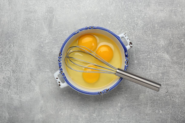 istock Whisk and eggs in pot on grey table, top view 1455706877