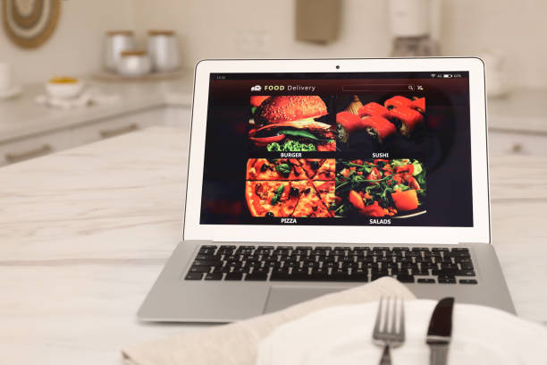 istock Modern laptop with open page for online food ordering on table in kitchen. Delivery service 1455707077