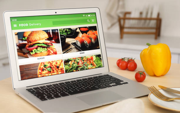 istock Modern laptop with open page for online food ordering on table in kitchen. Delivery service 1455707925