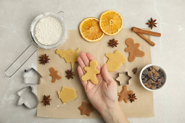 istock Woman holding unbaked cookie on light table, top view. Christmas biscuits 1455708003