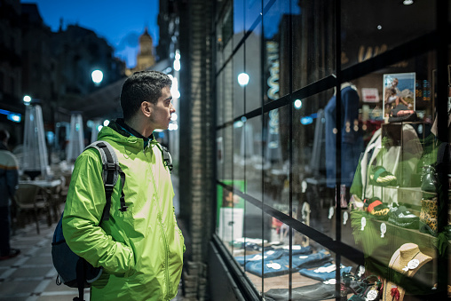 Man in a raincoat on a winter day looks at a shop window after taking a tour of the city