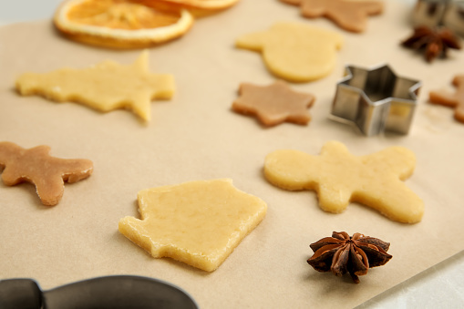 Unbaked cookies and cutters on parchment paper, closeup. Christmas biscuits