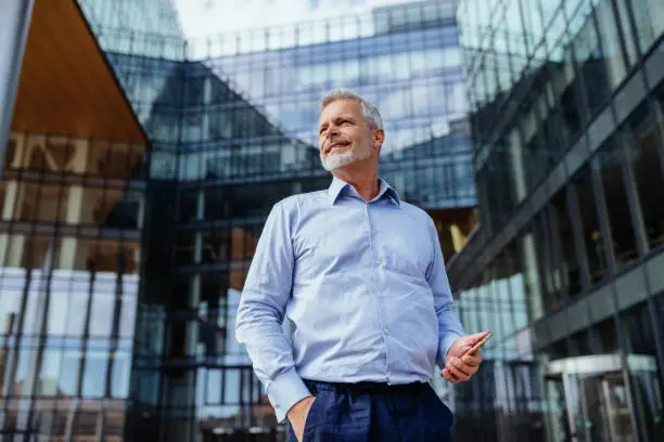 Senior businessman dressed in blue shirt in front of office building