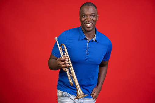 African american man sitting on a chair and holding trumpet in front of a red background