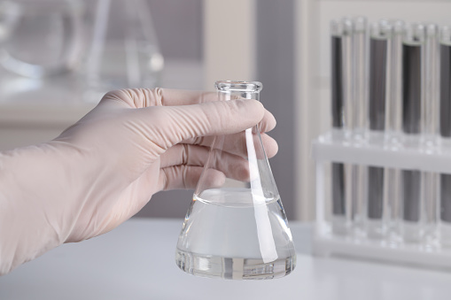 Scientist holding conical flask with transparent liquid in laboratory, closeup