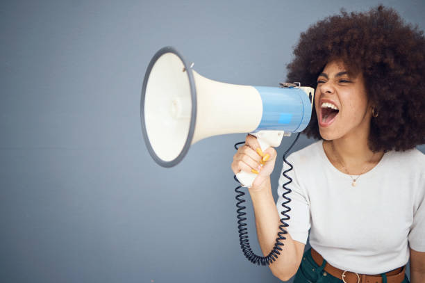 istock Studio, megaphone and angry black woman shouting and protesting for change, freedom or democracy. Loudspeaker, bullhorn and speech of young female using voice, screaming in protest for justice. 1455713094