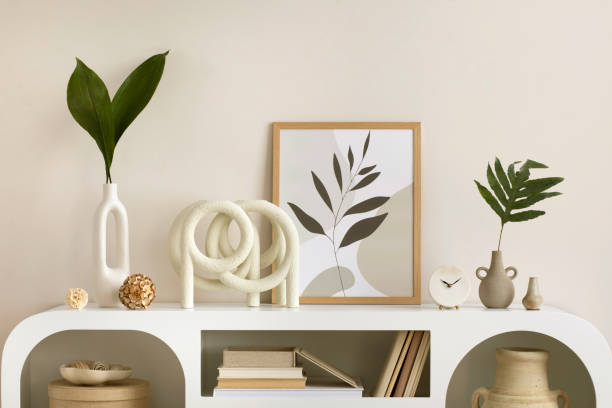 istock Interior design of harmonized living room with mock up poster frame, white commode, vase with leaves, decoration and personal accessories. Cozy home decor. Template. 1455713571