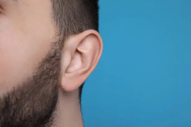 Man on light blue background, closeup of ear. Space for text