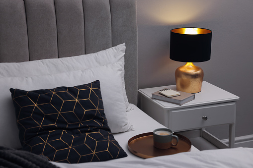 Stylish lamp and book on bedside table indoors. Bedroom interior element