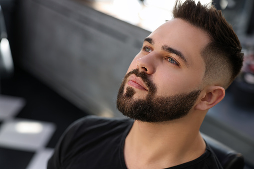 Handsome young man with fresh haircut and groomed beard in barbershop
