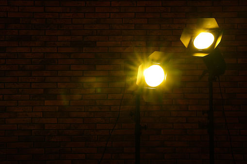 Bright yellow spotlights near brick wall in darkness, space for text