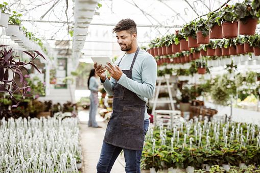 Young man gardener with digital tablet working in a garden center for better quality control. Environmentalist using digital tablet in greenhouse