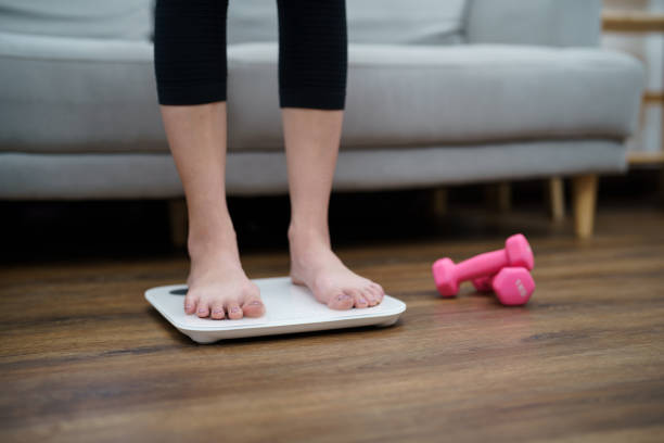 istock Fat diet and scale feet standing on electronic scales for weight control. Measurement instrument in kilogram for a diet control 1455717680