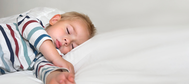 Young Child Sleeping on White Smooth Blanket. Little 3 Years Old Kids Sleeps Alone in Cozy Bedroom. Soft Textile. Sleepy Blonde Hair Baby Boy Dreaming in a Bed at home. Sign for banner. Space for text