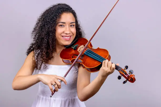 Photo of Smiling African girl playing violin at home over gray