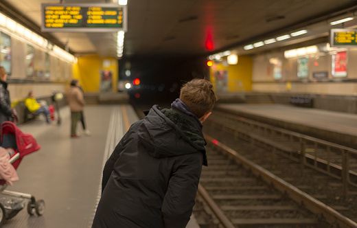 A teenager in a subway station looks out on the platform to see if the train is arriving.