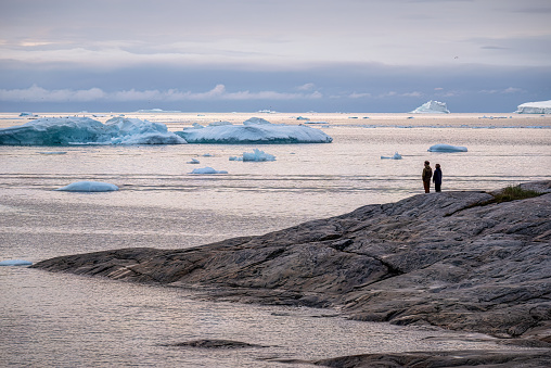 August 11, 2022 - Ilulissat, Greenland: Travel in arctic landscape nature with icebergs - Greenland tourist couple watching the enormous icebergs floating in the sea at Ilulissat Icefjord
