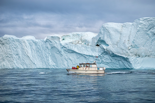 tourist boat with unrecognizable people sailing at night to see the midgnight sun and whales between the icebergs at Ilulissat Icefjord, Disko Bay, Greenland