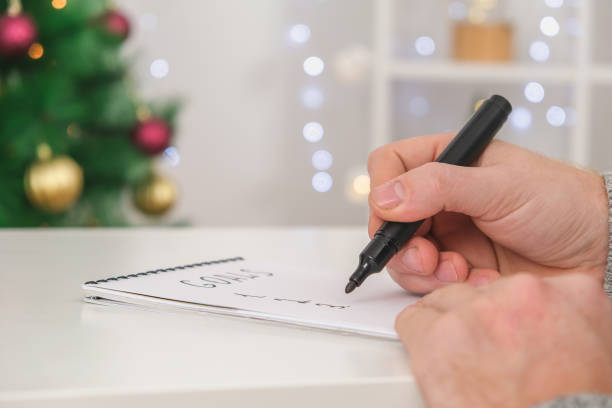 istock Man writes marker board white table with Christmas decor goals and plans new year and Christmas 2023. Goals New Year and Christmas written marker board. List wishes and goals new year and Christmas. 1455733677