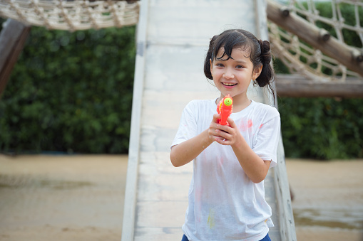 Happy child girl has fun playing sliding and shooting water gun on outdoor playground on hot summer day outdoors.