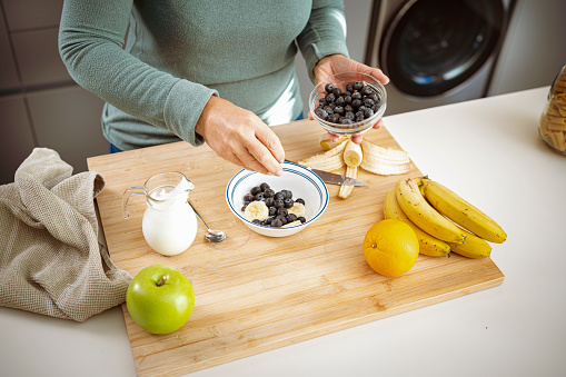 Healthy eating: mature woman preparing yogurt with fruits in domestic kitchen. High resolution 42Mp indoors digital capture taken with SONY A7rII and Zeiss Batis 40mm F2.0 CF lens