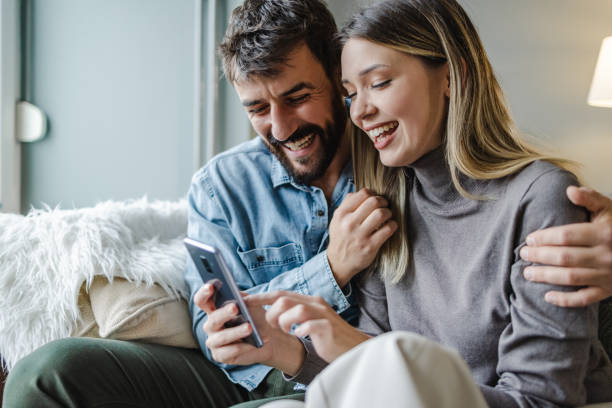Young couple embracing at home and using mobile phone