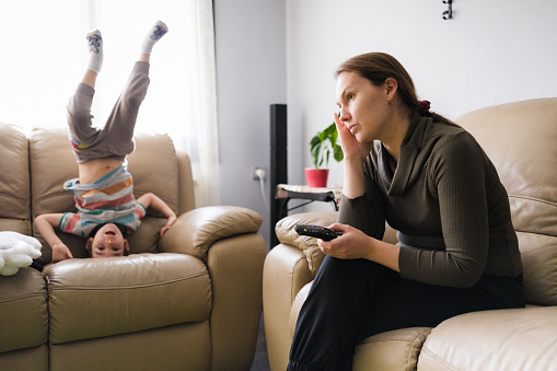 Little child boy distracts mother from watching TV and having some rest
