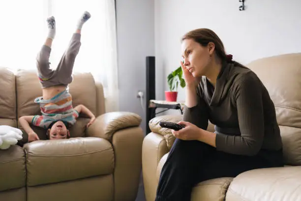 Photo of Little child boy distracts mother from watching TV and having some rest