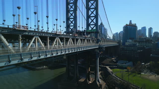 Forwards tight flight along subway train passing on Manhattan Bridge over East river. Large steel suspension bridge. New York City, USA