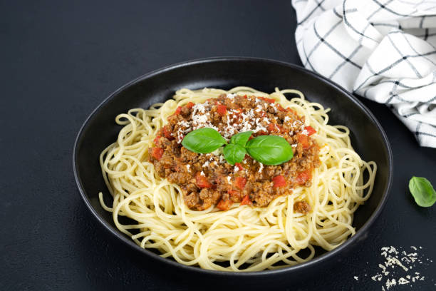 istock Spaghetti bolognese on a black plate with fresh basil and parmesan cheese on a black background. Italian food. 1455748526