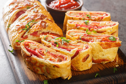Italian food Pizza roll stromboli with cheese, salami and tomatoes closeup on the wooden board on the table. Horizontal