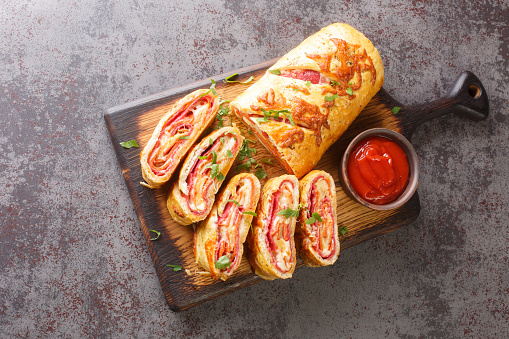 Italian stromboli, delicious pizza roll filled with sausage and ham closeup on the wooden board on the table. Horizontal top view from above
