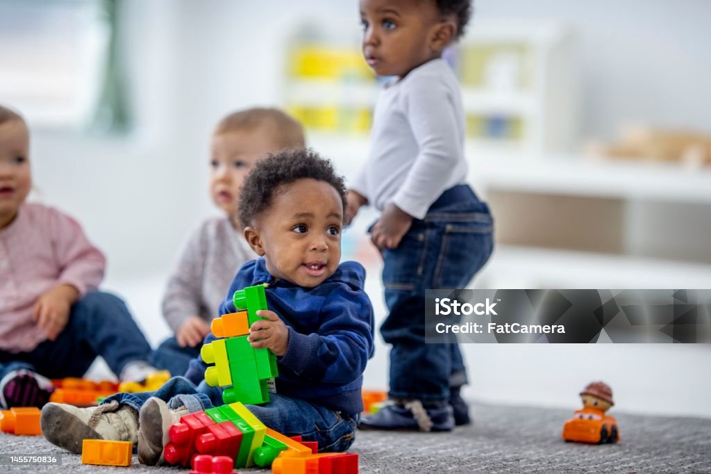Daycare Children Playing A small group of toddlers sit on the floor of their daycare classroom as they play together.  They are each dressed casually and are playing with colorful blocks. Baby - Human Age Stock Photo