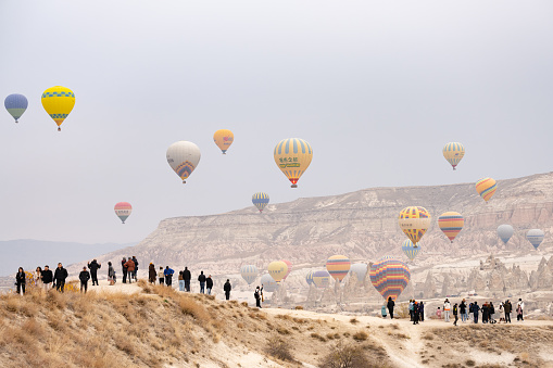 Goreme, Cappadocia, Turkey, January 10, 2023. Stunning view some people admiring some hot air balloons flying over the beautiful Cappadocia landscape.
