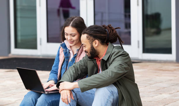istock Young multiracial couple using laptop on college campus 1455753448